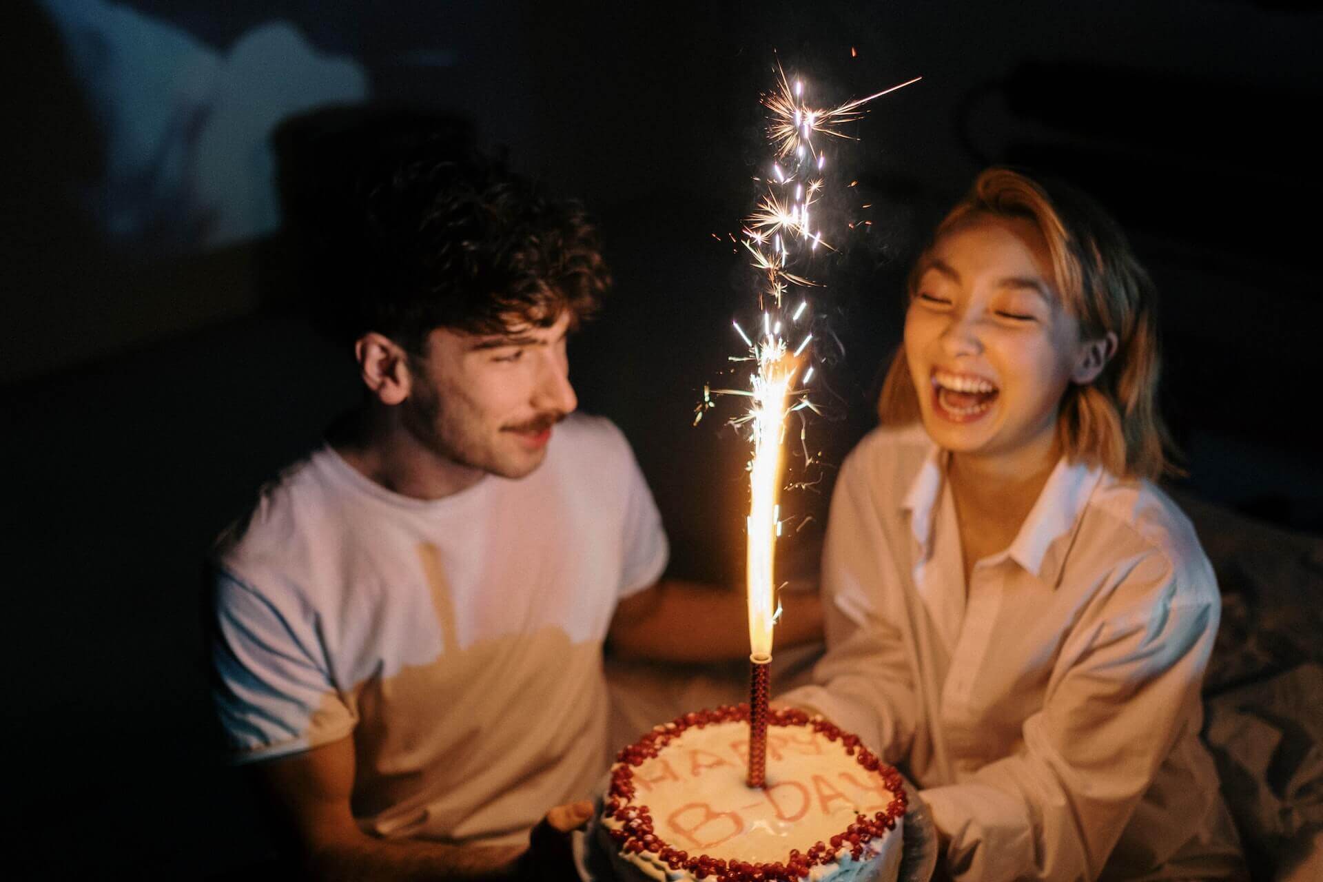 Man presents woman with birthday cake with sparkle.